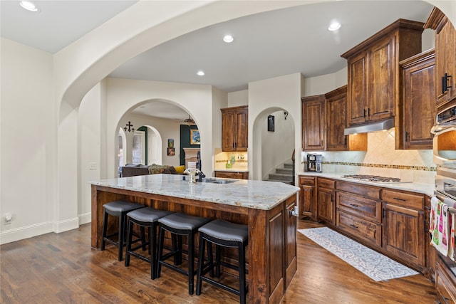 kitchen featuring light stone counters, appliances with stainless steel finishes, an island with sink, and dark hardwood / wood-style floors