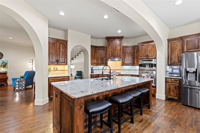 kitchen with stainless steel appliances, dark hardwood / wood-style flooring, tasteful backsplash, an island with sink, and light stone countertops