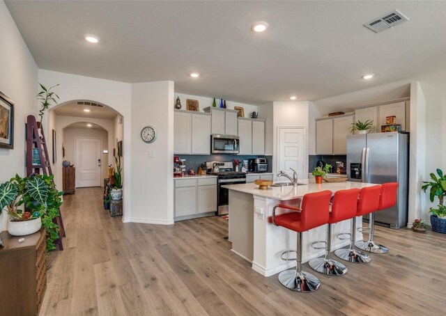 kitchen featuring a kitchen island with sink, a kitchen breakfast bar, light hardwood / wood-style flooring, decorative backsplash, and stainless steel appliances