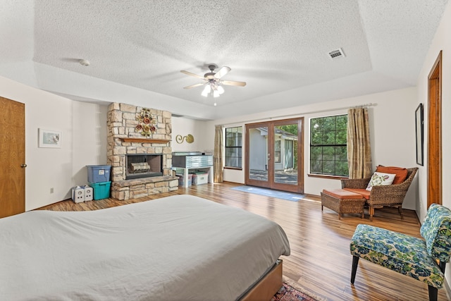 bedroom featuring light hardwood / wood-style floors, ceiling fan, a textured ceiling, a stone fireplace, and access to outside