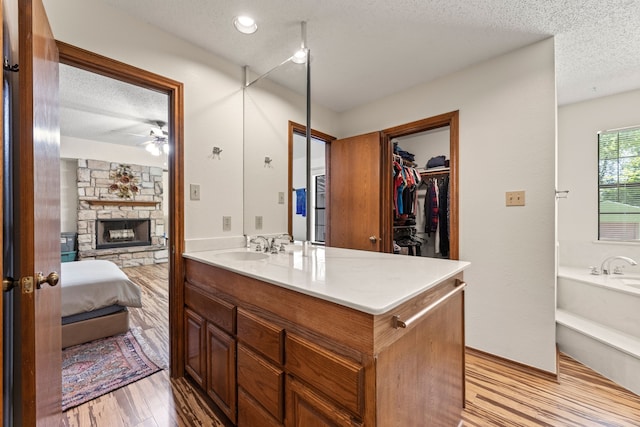 bathroom featuring ceiling fan, a textured ceiling, wood-type flooring, vanity, and a stone fireplace