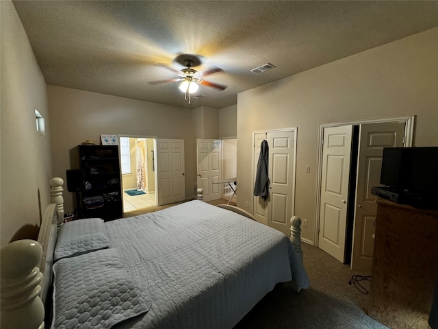 bedroom with a textured ceiling, light colored carpet, ceiling fan, and two closets