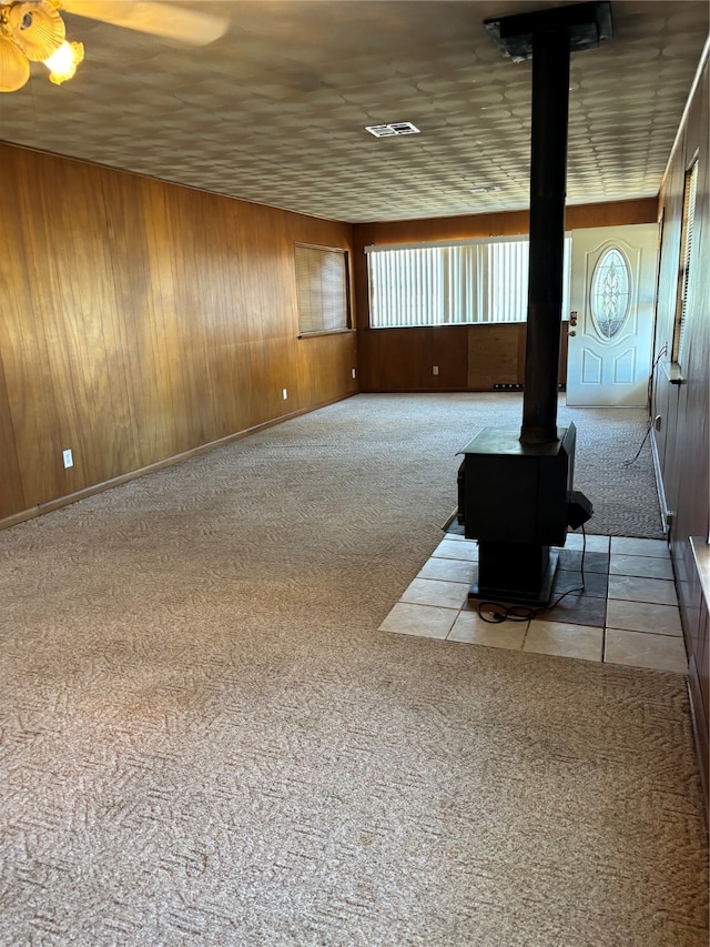 interior space with a wood stove, light colored carpet, wood walls, and ceiling fan