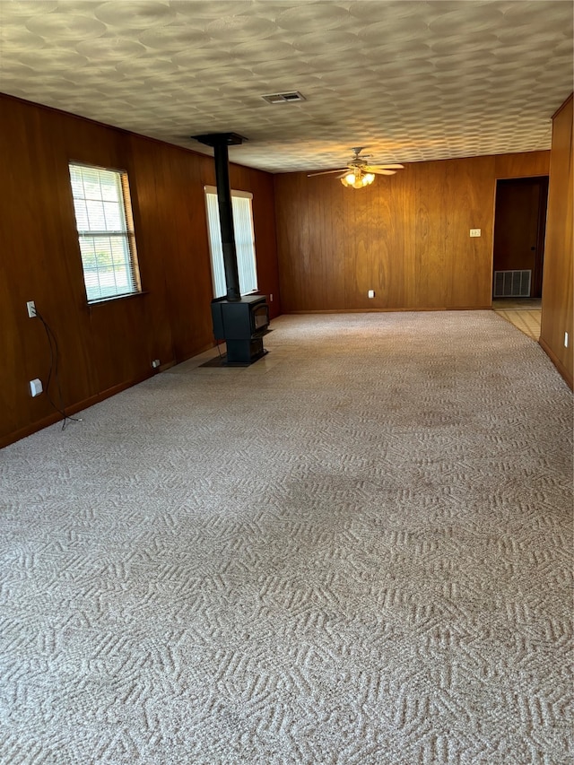 carpeted empty room featuring wood walls, a wood stove, and ceiling fan