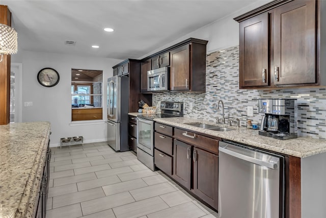 kitchen with light stone counters, stainless steel appliances, a sink, visible vents, and decorative backsplash