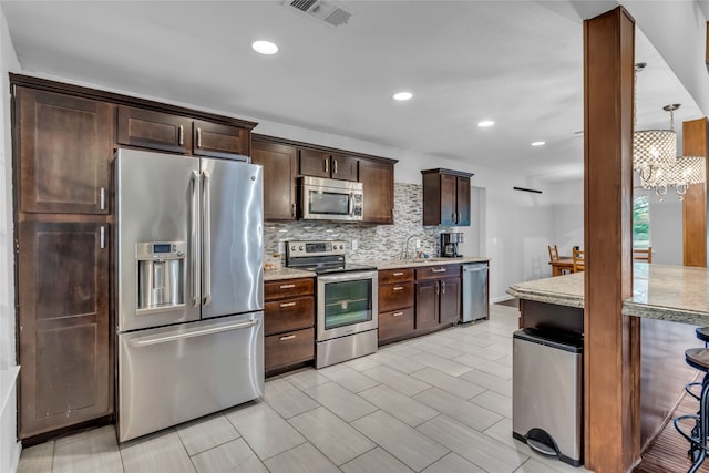 kitchen featuring tasteful backsplash, visible vents, appliances with stainless steel finishes, light stone counters, and decorative light fixtures