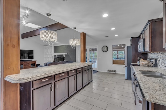 kitchen with lofted ceiling with beams, open floor plan, appliances with stainless steel finishes, light stone countertops, and decorative light fixtures