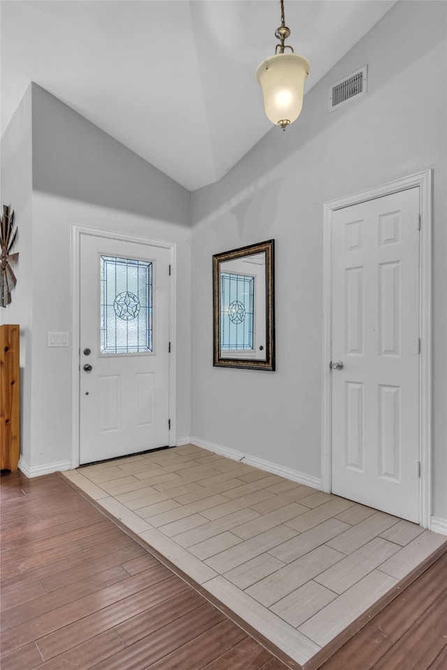 entrance foyer with light wood finished floors, baseboards, visible vents, and vaulted ceiling