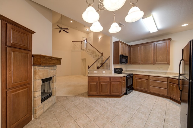 kitchen featuring black appliances, kitchen peninsula, hanging light fixtures, a stone fireplace, and light colored carpet