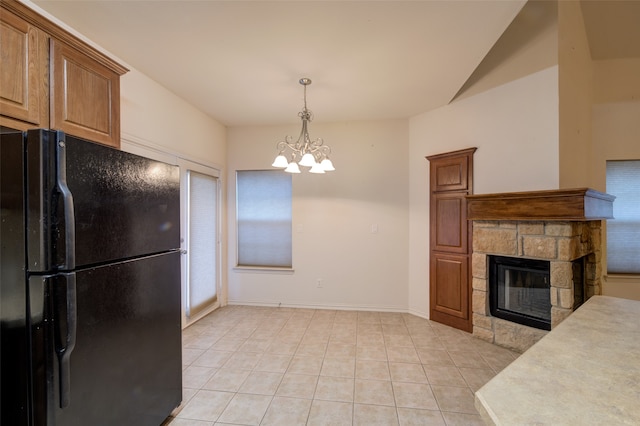 kitchen with black fridge, a stone fireplace, decorative light fixtures, light tile patterned floors, and an inviting chandelier