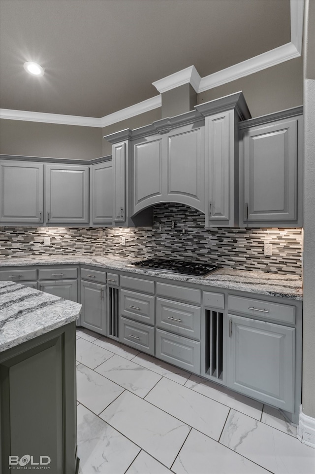 kitchen with light stone counters, stainless steel gas stovetop, crown molding, gray cabinetry, and decorative backsplash