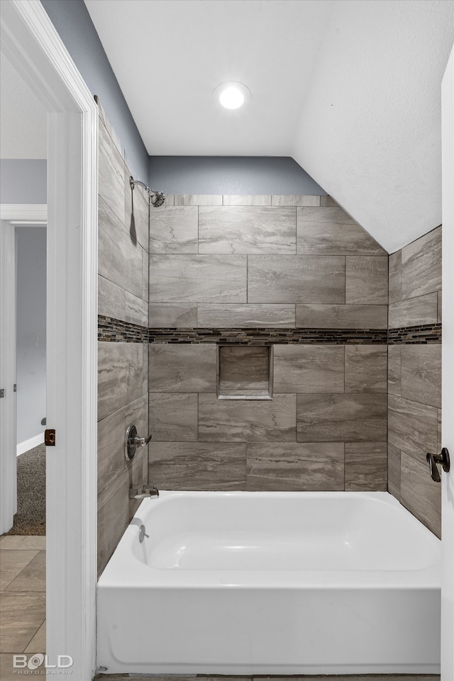 bathroom with tiled shower / bath combo, lofted ceiling, and tile patterned flooring