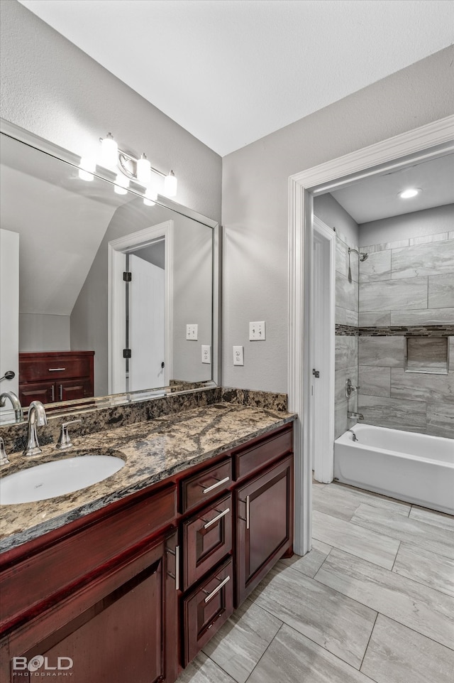 bathroom with tiled shower / bath, lofted ceiling, and vanity