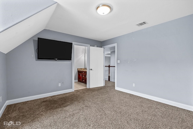 unfurnished bedroom with light colored carpet, lofted ceiling, and connected bathroom