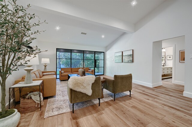 living room featuring beamed ceiling, light wood-type flooring, and high vaulted ceiling