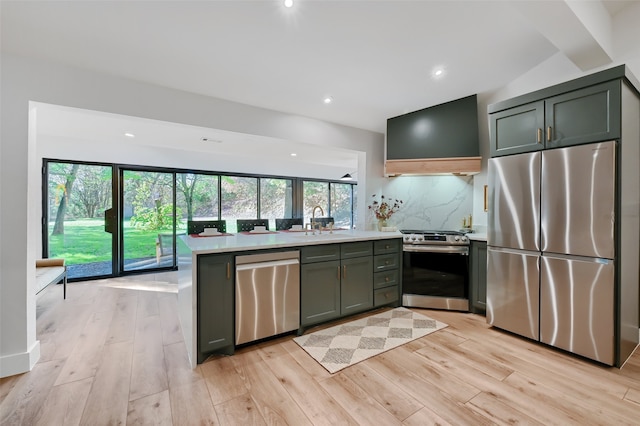 kitchen with sink, appliances with stainless steel finishes, backsplash, range hood, and light wood-type flooring