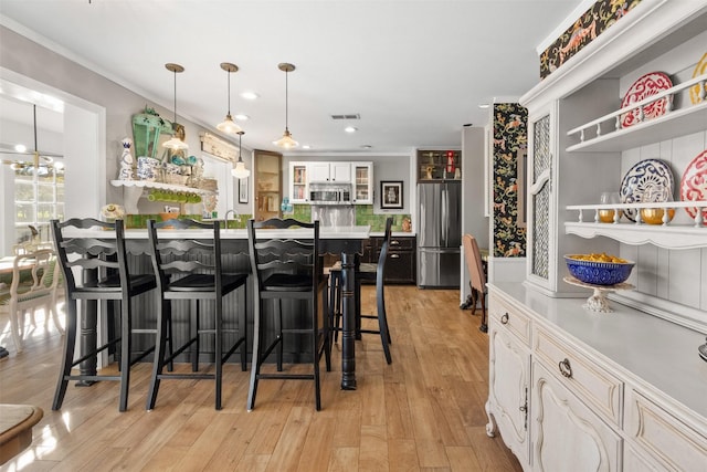7117 Serrano Dr, Benbrook, TX 76126 - kitchen featuring appliances with stainless steel finishes, a breakfast bar area, white cabinets, glass insert cabinets, and light wood-type flooring