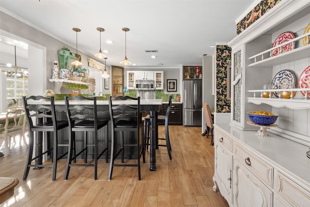 kitchen with stainless steel appliances, white cabinets, a kitchen breakfast bar, light wood-type flooring, and decorative light fixtures