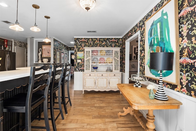 kitchen with hanging light fixtures, light hardwood / wood-style floors, stainless steel refrigerator, and a breakfast bar area