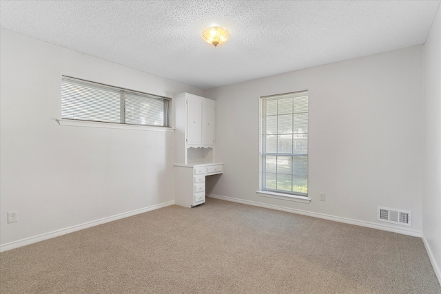 empty room featuring built in desk, a textured ceiling, and light carpet