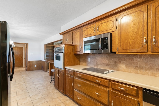 kitchen featuring appliances with stainless steel finishes, a textured ceiling, light tile patterned floors, wooden walls, and decorative backsplash