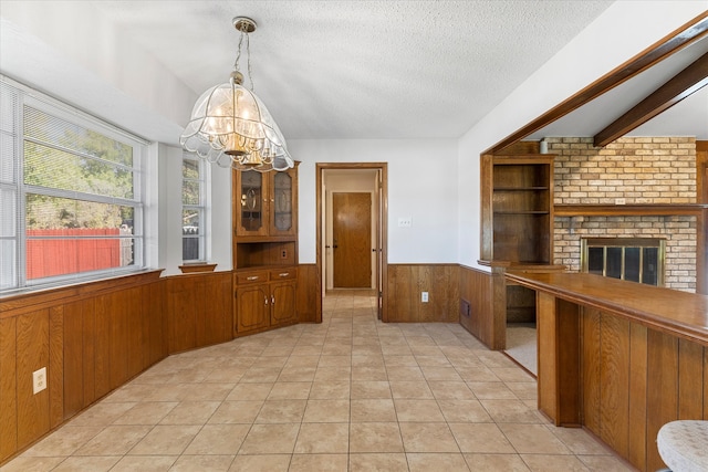 unfurnished dining area featuring wood walls, beamed ceiling, light tile patterned floors, a notable chandelier, and a brick fireplace