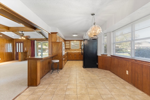 kitchen with black refrigerator, kitchen peninsula, light colored carpet, and a healthy amount of sunlight