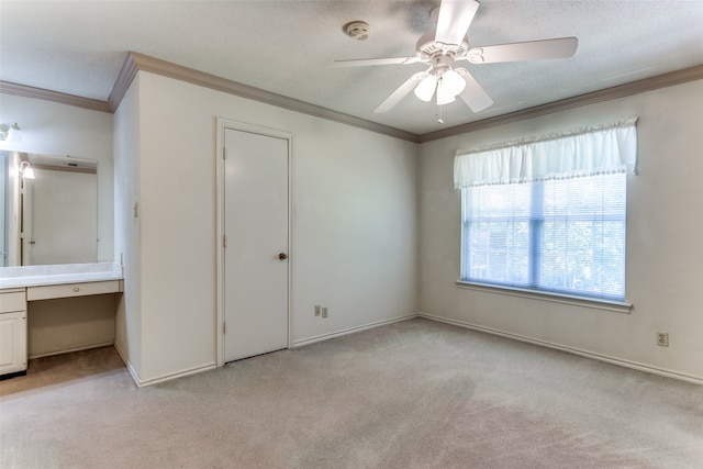 unfurnished bedroom with ornamental molding, light colored carpet, built in desk, and ceiling fan