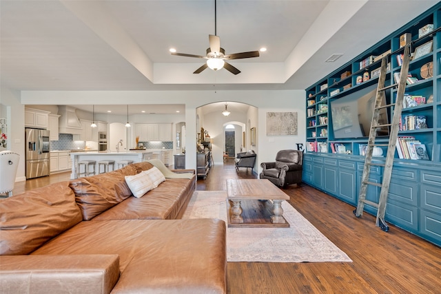 living room with a raised ceiling, ceiling fan, and light hardwood / wood-style flooring