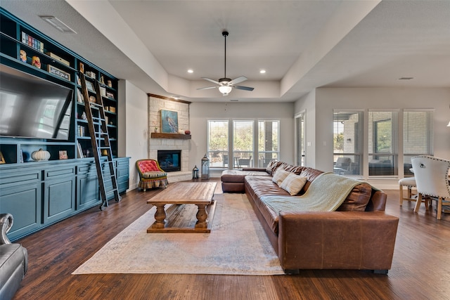 living room with a fireplace, ceiling fan, a raised ceiling, and dark hardwood / wood-style flooring