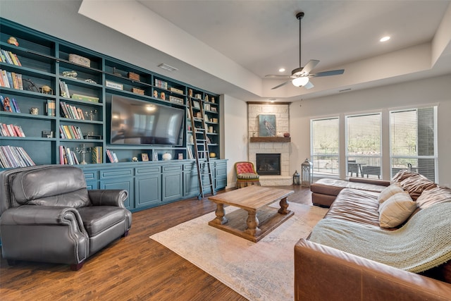 living room featuring ceiling fan, a tray ceiling, hardwood / wood-style floors, a fireplace, and built in features