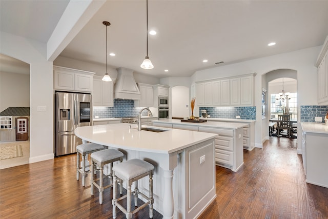 kitchen with dark hardwood / wood-style flooring, a center island with sink, sink, custom exhaust hood, and appliances with stainless steel finishes