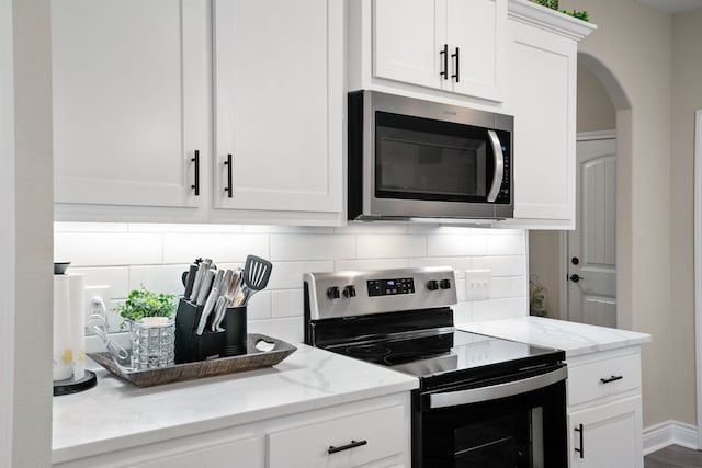 kitchen featuring white cabinetry, decorative backsplash, appliances with stainless steel finishes, and light stone countertops