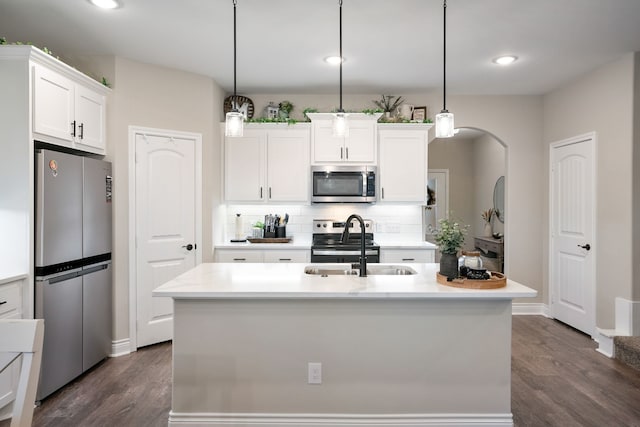 kitchen featuring white cabinets, appliances with stainless steel finishes, a center island with sink, and decorative light fixtures