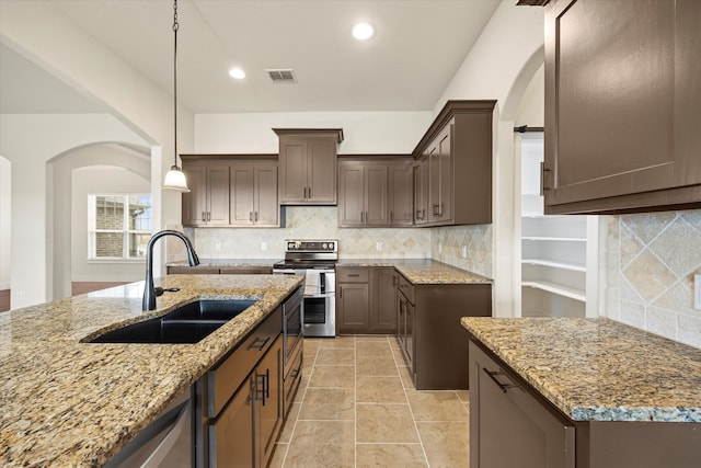 kitchen with stainless steel range with electric cooktop, a center island with sink, pendant lighting, light stone countertops, and sink