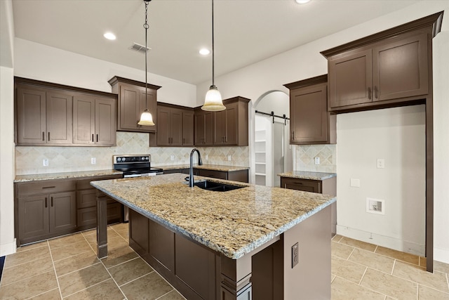 kitchen featuring sink, light stone counters, a barn door, and an island with sink