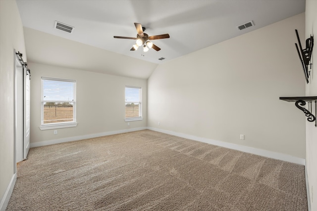 carpeted empty room with a barn door, vaulted ceiling, and ceiling fan