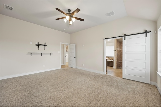 unfurnished bedroom with connected bathroom, a barn door, vaulted ceiling, light colored carpet, and ceiling fan