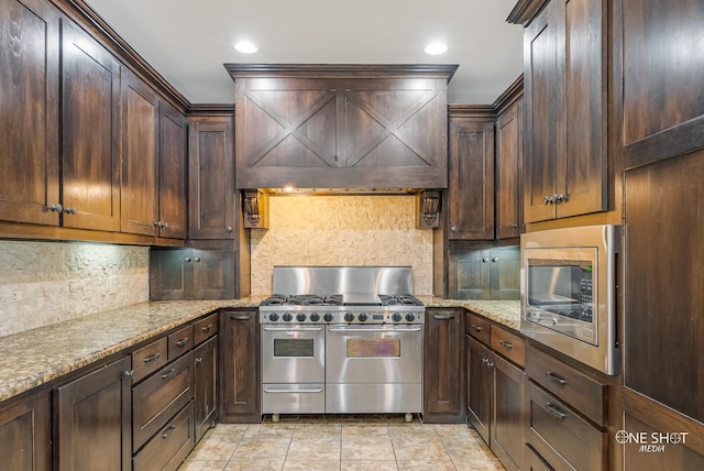 kitchen featuring premium range hood, light stone counters, appliances with stainless steel finishes, dark brown cabinetry, and decorative backsplash