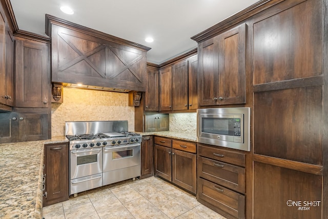 kitchen featuring tasteful backsplash, light stone countertops, premium range hood, and stainless steel appliances