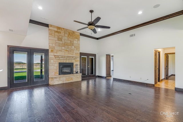 unfurnished living room with a stone fireplace, french doors, hardwood / wood-style flooring, ceiling fan, and a high ceiling