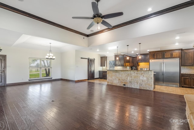 unfurnished living room with ceiling fan with notable chandelier, dark hardwood / wood-style flooring, a barn door, and crown molding