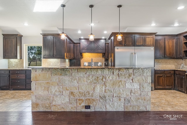 kitchen featuring dark brown cabinets, high end fridge, hanging light fixtures, and light stone counters