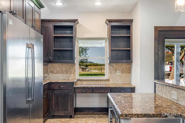 kitchen featuring tasteful backsplash, stainless steel fridge, dark stone counters, dark brown cabinets, and light tile patterned floors