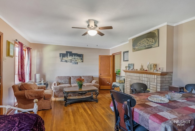 living room featuring ceiling fan, wood-type flooring, ornamental molding, and a brick fireplace