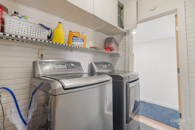 clothes washing area with washing machine and dryer and wood walls