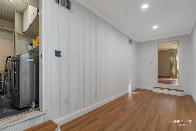 interior space with crown molding, hardwood / wood-style floors, wood walls, and washer / dryer