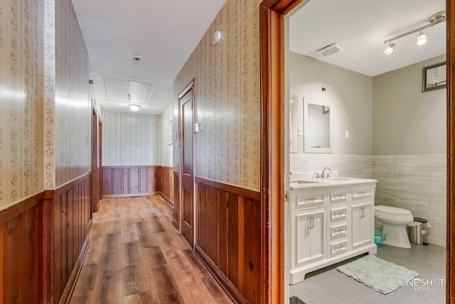 corridor featuring light hardwood / wood-style floors, track lighting, wooden walls, and sink