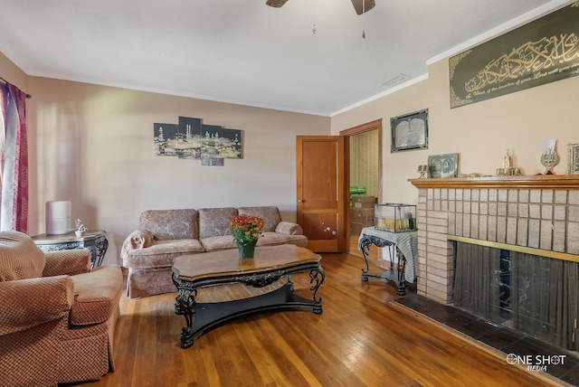 living room featuring wood-type flooring, ornamental molding, ceiling fan, and a fireplace