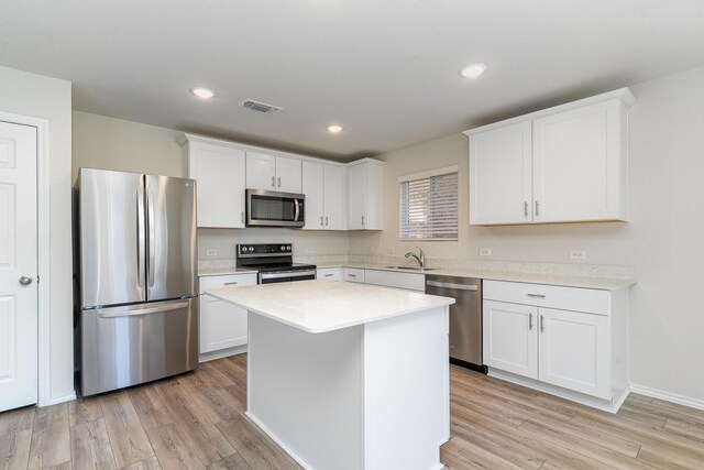 kitchen with appliances with stainless steel finishes, light wood-type flooring, white cabinetry, and a kitchen island